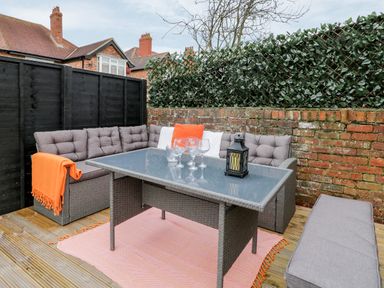 An outdoor seating area with a gray wicker sofa set table with glass top and cushions on a wooden deck at Beach House in Bridlington