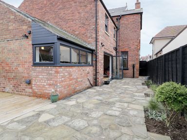 A stone patio with potted plants beside a brick house with an open door and a black fence at Beach House in Bridlington