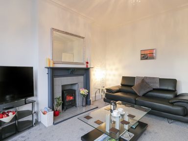 A living room with a black leather sofa, glass coffee table, electric fireplace, flat screen TV, and a floor lamp at Beach House in Bridlington