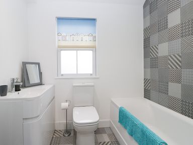 A bathroom with a toilet, bathtub, sink with mirror, patterned tiles, and a window blind at Beach House in Bridlington