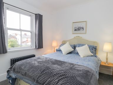 A bedroom with a double bed two pillows two bedside lamps a window with curtains and a framed picture on the wall at Beach House in Bridlington