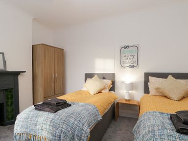 A bedroom with two single beds a wooden wardrobe a bedside table with a lamp and a wall decoration at Beach House in Bridlington