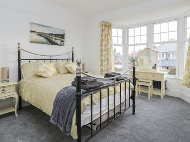 A bedroom with a metal bed frame bedside tables a dressing table with mirror and windows at Beach House in Bridlington