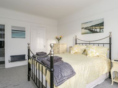 A bedroom with a metal bed frame yellow bedding two folded gray towels on the bed a white door beside a chest of drawers with flowers and paintings on the walls at Beach House in Bridlington