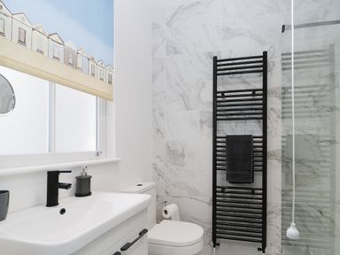A bathroom with a sink, toilet, black towel rail, and window with a patterned blind at Beach House in Bridlington