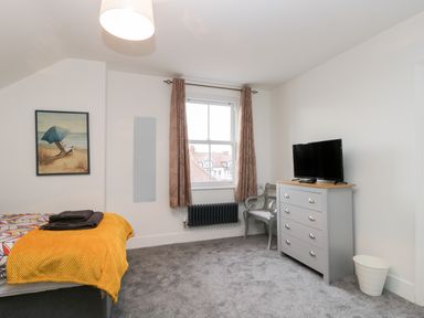 A bedroom with a bed a yellow throw a window with curtains a grey chest of drawers a chair and a television at Beach House in Bridlington