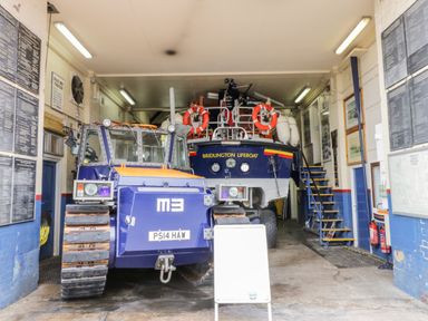 A blue tracked vehicle and a lifeboat inside a garage with plaques on the walls at Bridlington Lifeboat Station