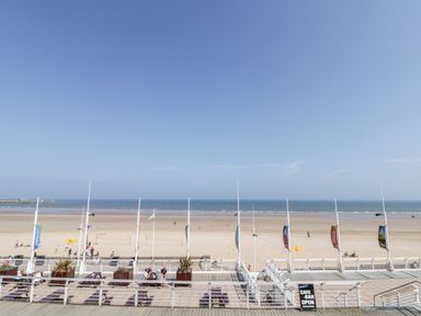 A beach with people walking and sitting near a boardwalk with flags and benches at Beach House in Bridlington
