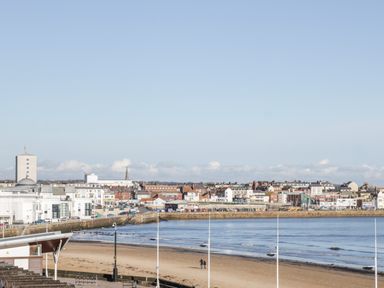 A sandy beach with two people walking near the shoreline and a town with buildings along the coast at Beach House in Bridlington