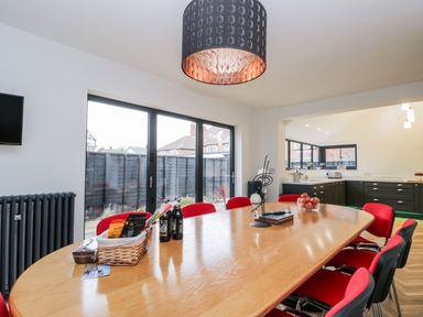 A dining room with a wooden table surrounded by red chairs and a kitchen with black cabinets in the background at Beach House in Bridlington