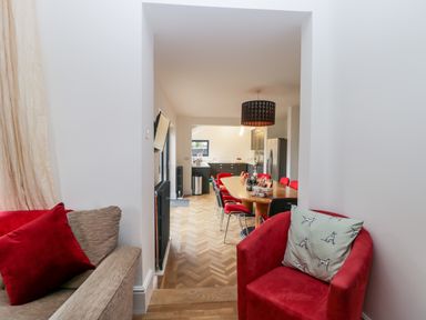 A dining area with a long wooden table surrounded by red chairs a black hanging light and a kitchen in the background seen from a living room with a red armchair and beige sofa with red cushion at Beach House in Bridlington