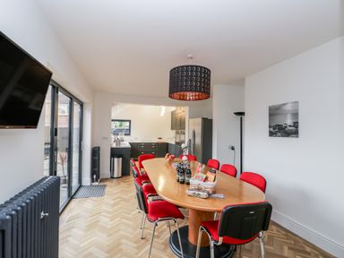 A dining area with a wooden table surrounded by red chairs next to a kitchen with dark cabinets and large sliding glass doors at Beach House in Bridlington