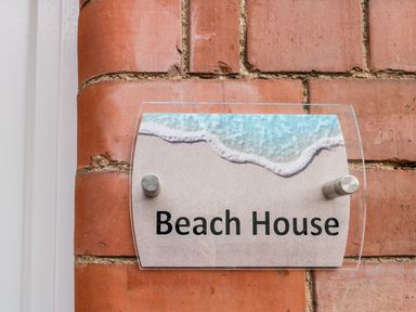 A glass sign with a beach design and the text Beach House mounted on a red brick wall at Beach House in Bridlington