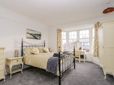 A bedroom with a black metal bed frame yellow bedding cream furniture and bay windows with patterned curtains at Beach House in Bridlington