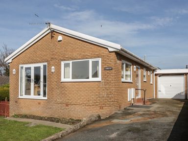 A brick house with white windows and a driveway leading to a garage at Arwelfa in Penmaenmawr