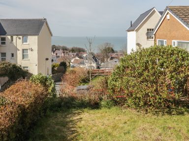 A garden with bushes and grass between two houses with a sea view at Arwelfa in Penmaenmawr