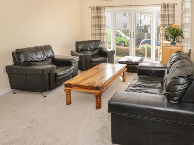 A living room with black leather sofas a wooden coffee table and a flower vase on a cabinet at Arwelfa in Penmaenmawr