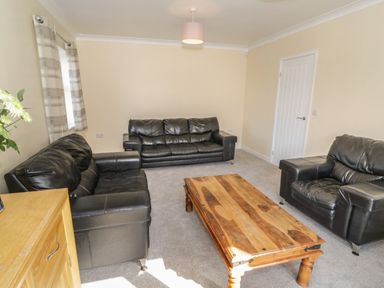 A living room with black leather sofas a wooden coffee table and a wooden cabinet with flowers at Arwelfa in Penmaenmawr