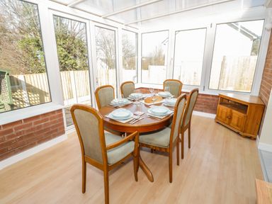 A dining area with a wooden table set for six with plates glasses and cutlery next to large windows at Arwelfa in Penmaenmawr