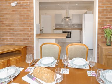 A dining table set with plates glasses cutlery and bread with a kitchen in the background at Arwelfa in Penmaenmawr