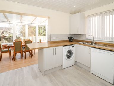 A kitchen with wooden countertops white cabinets a washing machine dishwasher and dining area with table and chairs at Arwelfa in Penmaenmawr