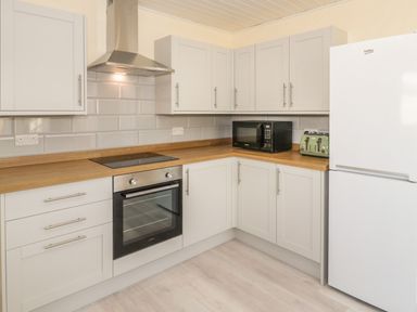 A kitchen with white cabinets a wooden countertop a black oven microwave a green toaster and a white refrigerator at Arwelfa in Penmaenmawr