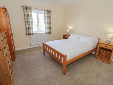 A bedroom with a wooden bed white bedding two bedside tables with lamps a wooden wardrobe and chest of drawers at Arwelfa in Penmaenmawr