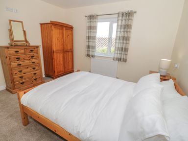 A bedroom with a wooden bed a wooden dresser with a mirror wooden wardrobe and a window with curtains at Arwelfa in Penmaenmawr