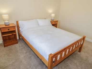 A bedroom with a wooden double bed with white bedding and two wooden bedside tables with lamps at Arwelfa in Penmaenmawr