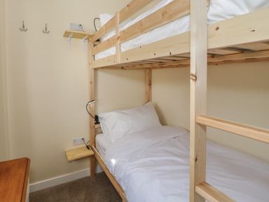 A bedroom with a wooden bunk bed a small wall shelf hooks and a bedside lamp at Arwelfa in Penmaenmawr