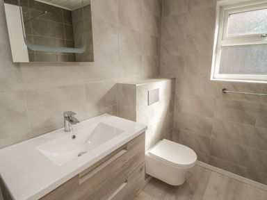 A bathroom with a sink and cabinet a wall-mounted toilet and a window at Arwelfa in Penmaenmawr