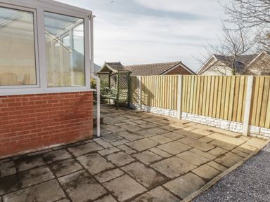 A paved outdoor area with a wooden fence and a green wooden bench at Arwelfa in Penmaenmawr