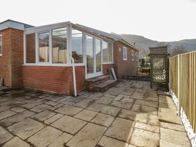 A paved backyard area with a brick building and glass conservatory and wooden fence at Arwelfa in Penmaenmawr