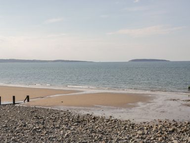 A rocky and sandy beach leading to a calm sea with two islands visible in the distance at Arwelfa in Penmaenmawr