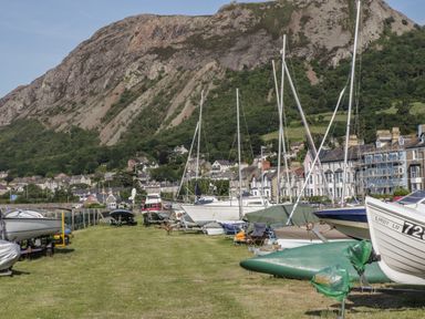 A grassy area with boats on trailers near houses and a large rocky hill in the background at Arwelfa in Penmaenmawr