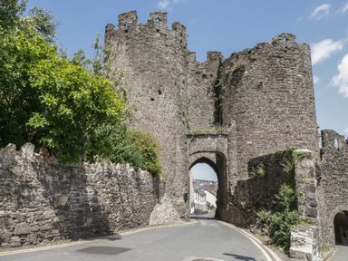 A stone castle gate with an archway over a road and green trees on the side at Arwelfa in Penmaenmawr