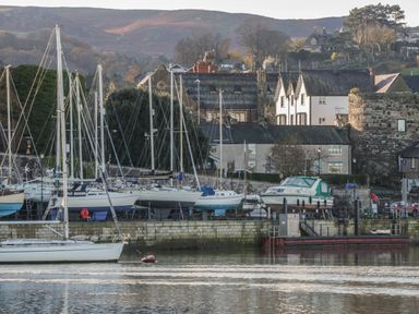A marina with sailboats docked near stone buildings and hills in the background at Arwelfa in Penmaenmawr
