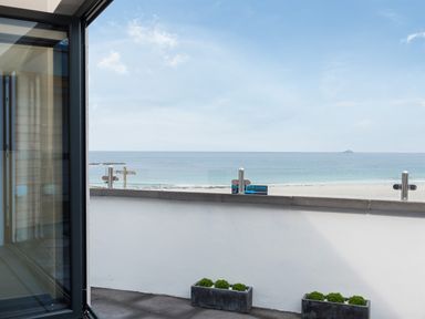 A balcony with potted plants overlooking a beach and ocean at The Old Beach Store in Sennen Cove