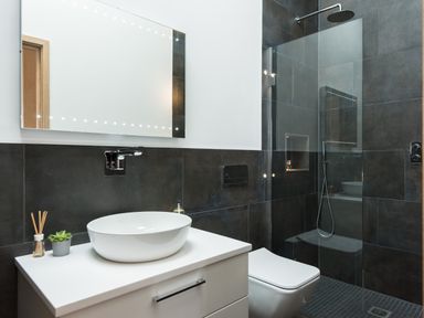 A bathroom with a wall-mounted sink, mirror, toilet, and glass-enclosed shower at The Old Beach Store in Sennen Cove