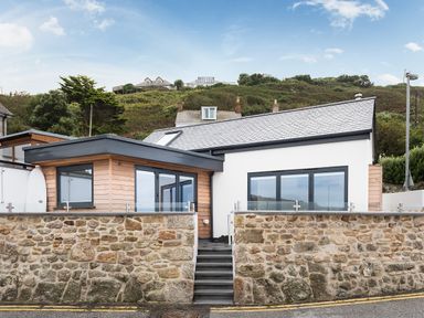 A modern house with stone walls wooden cladding and large windows by a hillside at The Old Beach Store in Sennen Cove