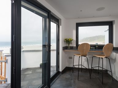 A small dining area with two wooden chairs and a countertop by a window overlooking a beach and ocean