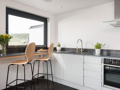 A kitchen with two wooden bar stools by a counter and a window overlooking a hill at The Old Beach Store in Sennen Cove