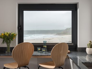A kitchen counter with two wooden chairs and a window showing a beach view at The Old Beach Store in Sennen Cove