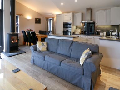 A living room with a gray sofa a dining table with black chairs and a kitchen area at Tarn Lodge in Bowness-On-Windermere