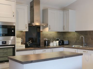 A kitchen with white cabinets wooden countertops a sink toaster kettle coffee machine and built in oven at Tarn Lodge in Bowness-On-Windermere