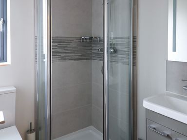 A bathroom with a glass shower enclosure a toilet a sink and a window at Tarn Lodge in Bowness-On-Windermere
