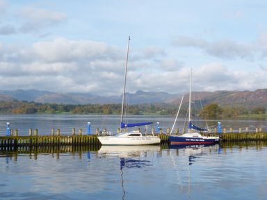 Two sailboats docked at a wooden pier with water and hills in the background at Tarn Lodge in Bowness-On-Windermere