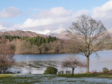 A lake with trees along the shore and snow covered mountains in the background at Tarn Lodge in Bowness-On-Windermere