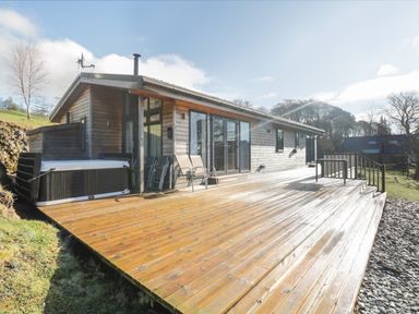 A wooden deck with chairs and a hot tub outside a wooden house at Tarn Lodge in Bowness-On-Windermere