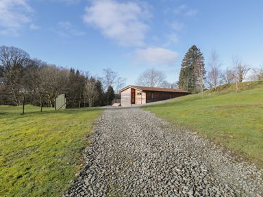A gravel pathway leading to a wooden house surrounded by grass and trees at Tarn Lodge in Bowness-On-Windermere